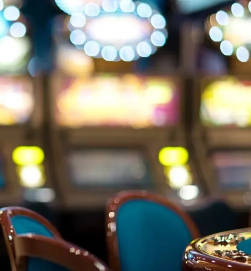Blurred image of empty blue casino chairs in front of brightly lit slot machines, with colorful circular lights in the background creating a vibrant gaming atmosphere—perfect for guests visiting from a nearby Torch Lake bed and breakfast.
