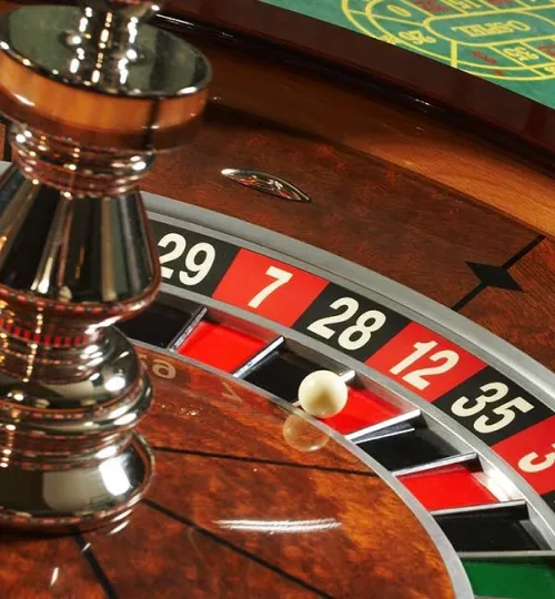 A close-up of a roulette wheel at a charming Torch Lake bed and breakfast shows the ball landed on red number 7. The shiny metal spindle, wooden surface, and sections of black, red, and green slots are clearly visible.