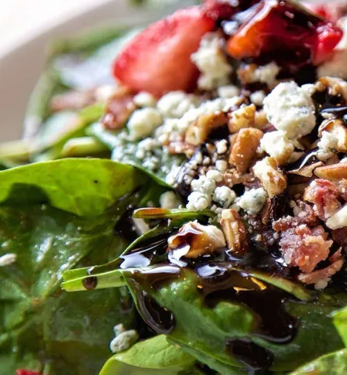 Close-up of a fresh spinach salad topped with crumbled blue cheese, chopped pecans, sliced strawberries, and drizzled with a dark balsamic glaze—perfect for enjoying at a cozy Torch Lake bed and breakfast.