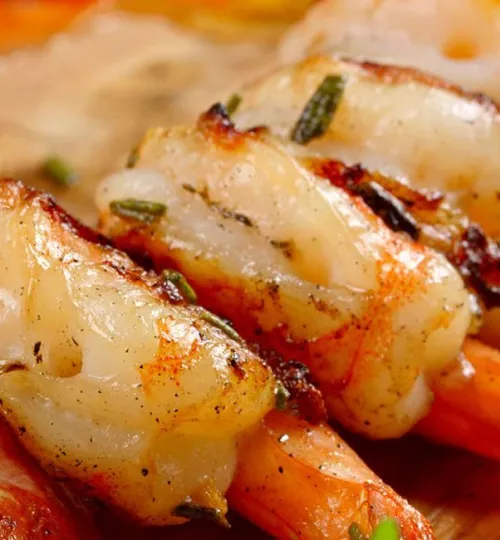 Close-up of grilled shrimp tails seasoned with herbs, showing juicy, tender meat with a slightly charred exterior—perfect for savoring at a cozy bed and breakfast near Torch Lake.