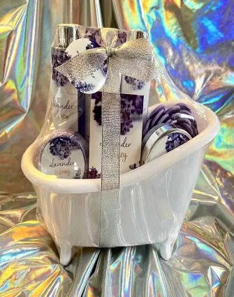 A small white ceramic bathtub holds lavender-themed bath products and soaps, wrapped with a silver ribbon, set against a shiny holographic background—perfect for a relaxing retreat reminiscent of a torch lake bed and breakfast.