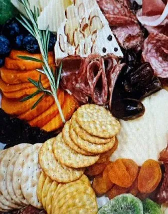 A charcuterie board with sliced salami, crackers, assorted cheeses, dried apricots, figs, fresh blueberries, black olives, and a sprig of rosemary—perfect for enjoying at a cozy bed and breakfast near Torch Lake.