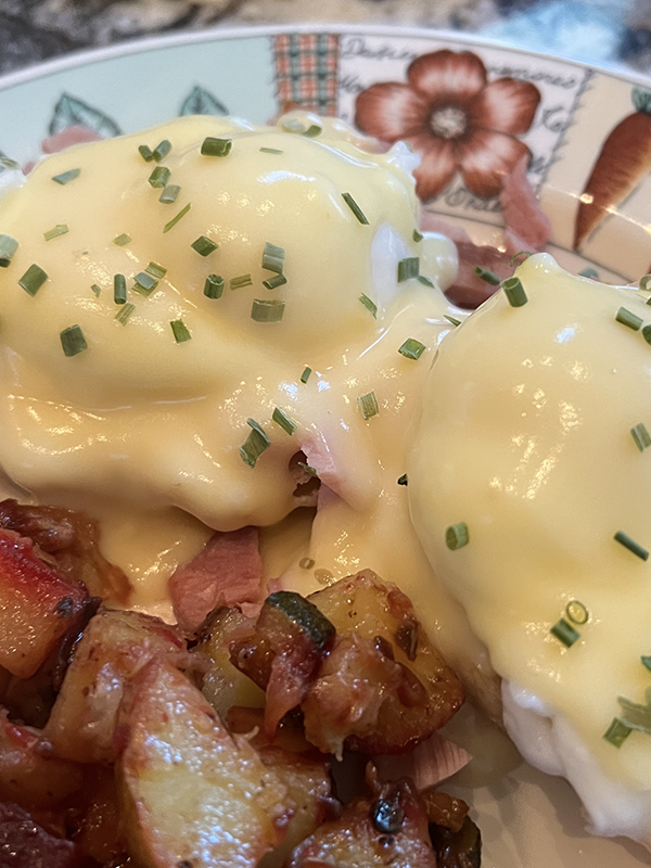 Close-up of eggs benedict topped with creamy hollandaise sauce and chives, served with browned seasoned potatoes on a colorful plate—a perfect bed and breakfast delight near the shores of Torch Lake.